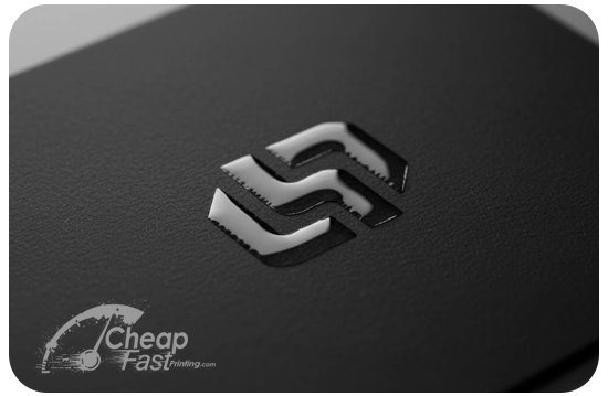 An extreme close-up, macro photograph of a Spot UV business card. The card itself is a deep, matte black. A logo is printed on it using raised Spot UV, making it shiny and tactile. The lighting is angled to catch the reflection on the Spot UV elements, clearly contrasting them against the matte background.